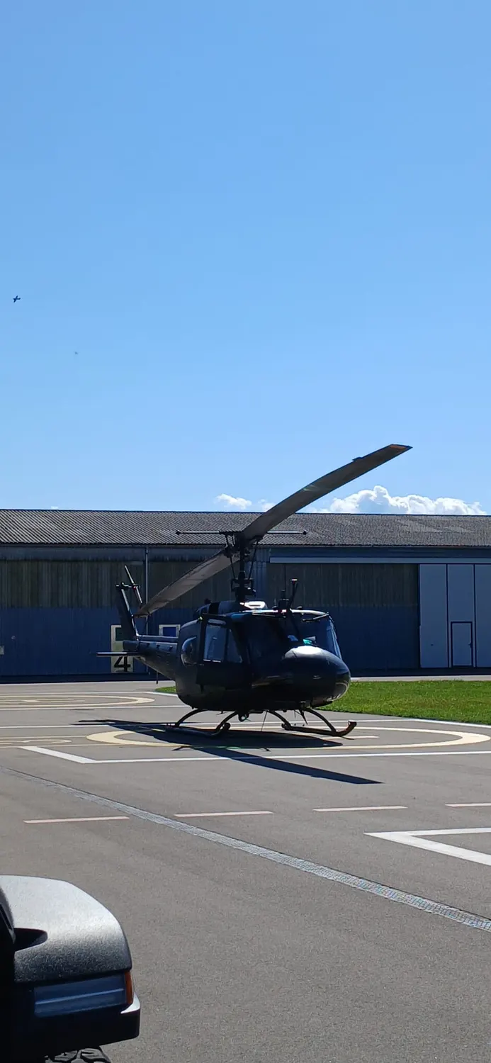 A Bell UH-1 helicopter standing on the apron in front of the hangars, rotor blade drooping