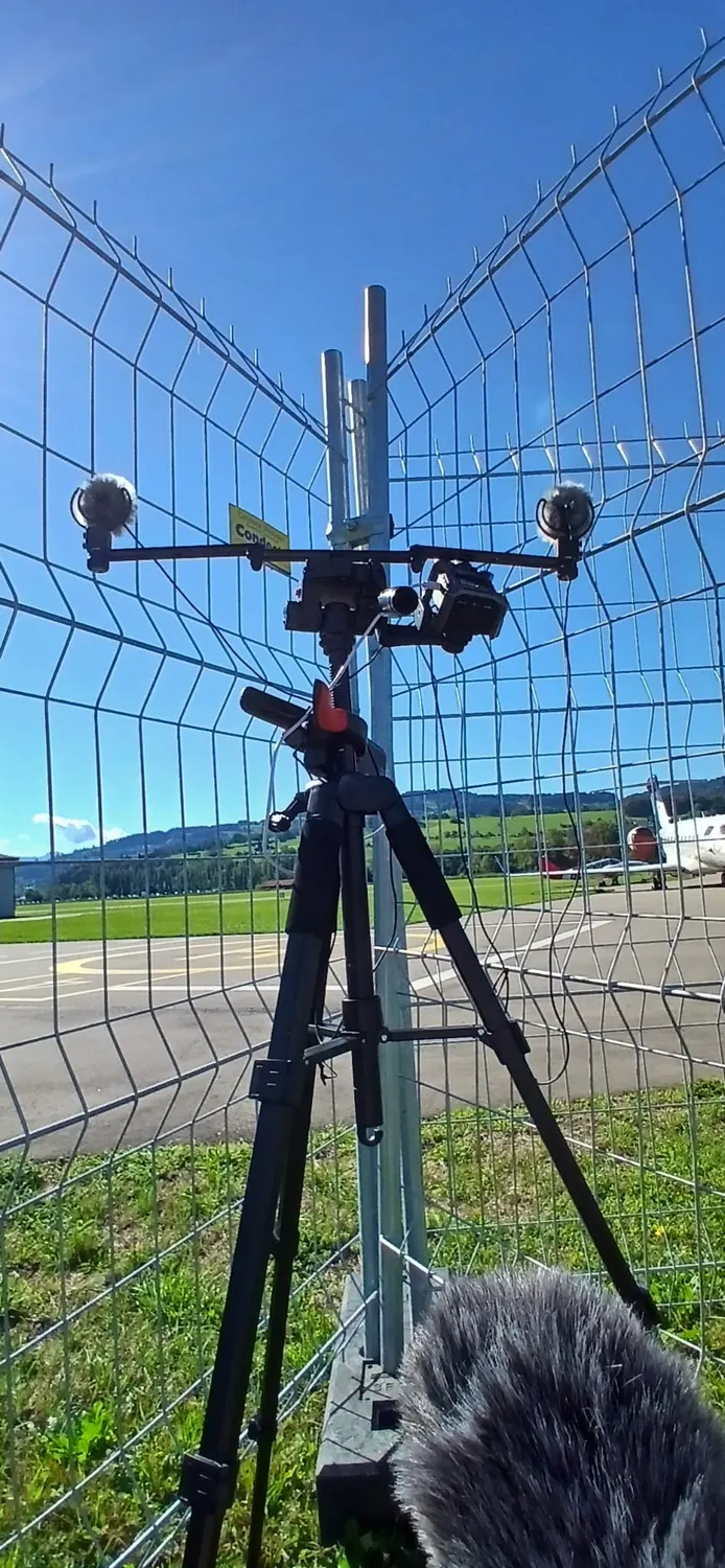 The recorder and a pair of microphones clamped to the perimeter fence of the airfield, mountains behind