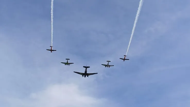 Five propeller aircraft in formation with two smoke trails against a blue sky at the Altenrhein air show