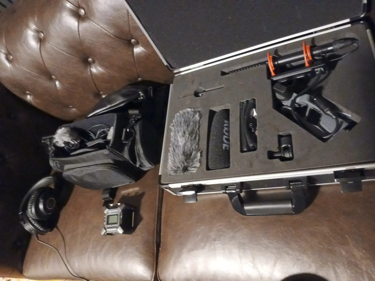 An open flight case with a shotgun microphone, its suspension and pistol grip, a blimp windshield, a recorder bag and headphones