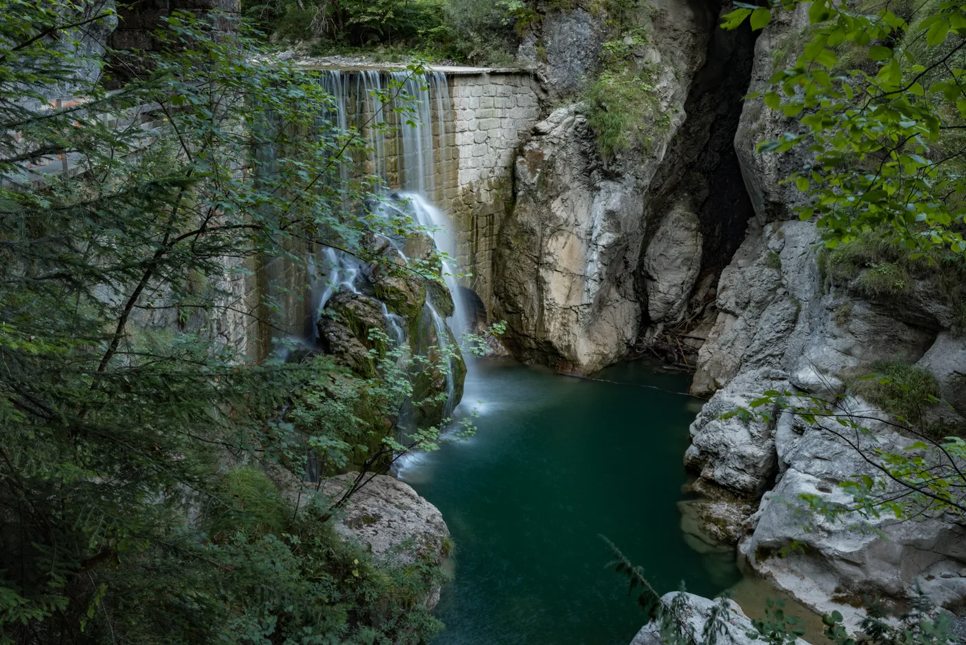 A waterfall dropping over a rock ledge into a green pool inside a narrow limestone gorge