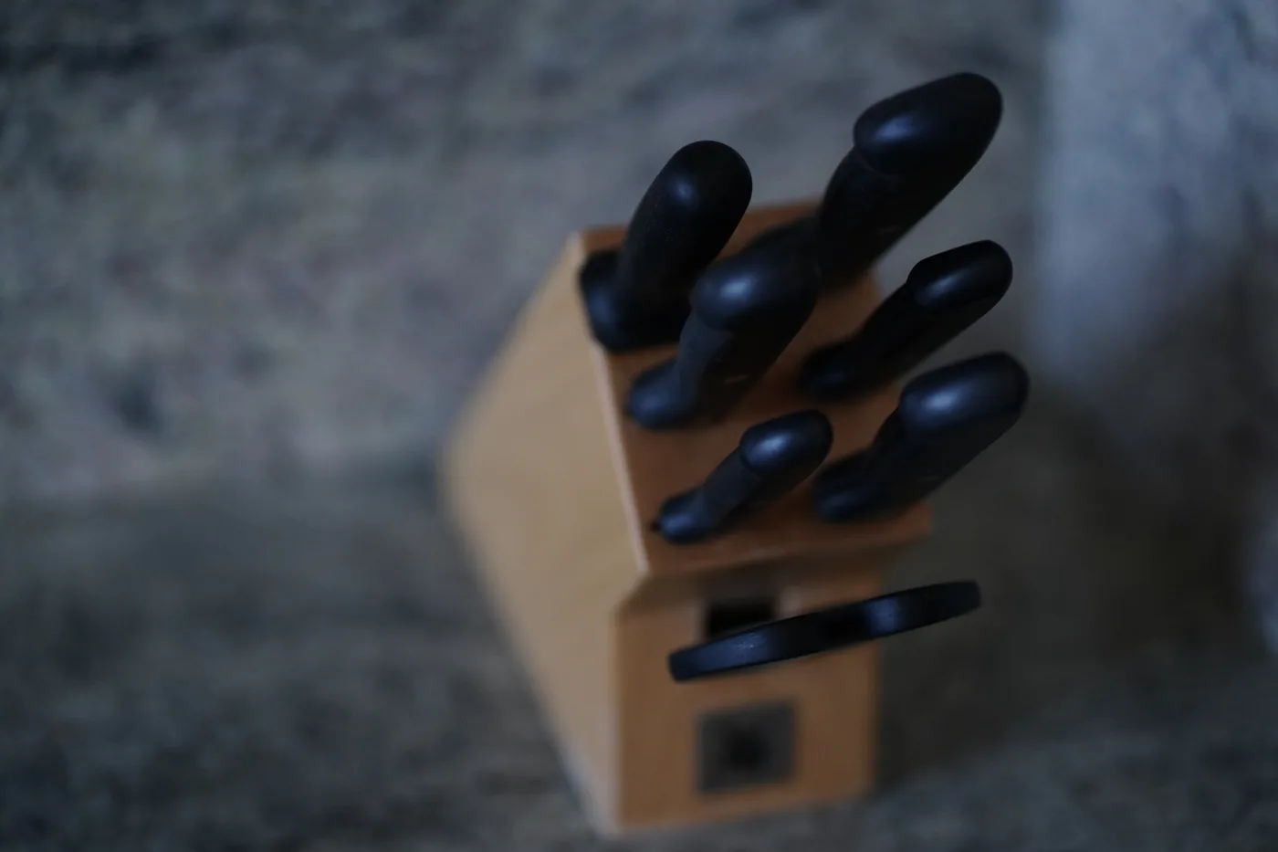 A wooden knife block seen from above, six black handles standing in it