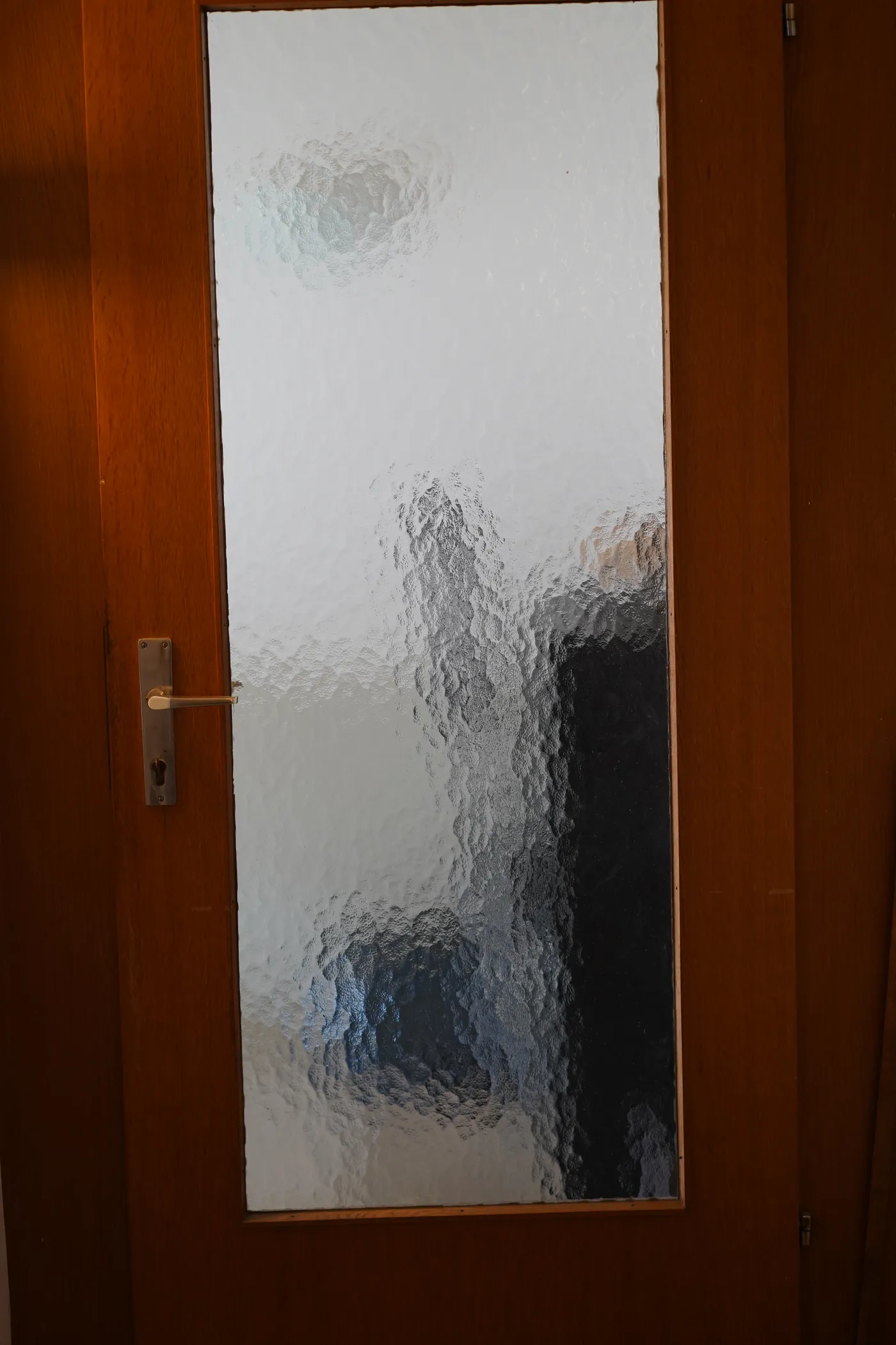 A wooden cellar door with a brass handle and frosted glass