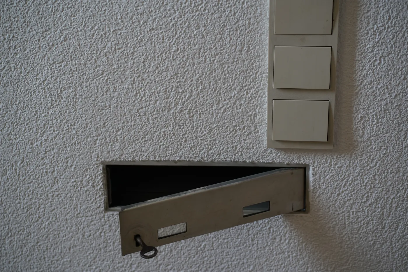 A metal letterbox flap set into a wall, doorbell buttons above it
