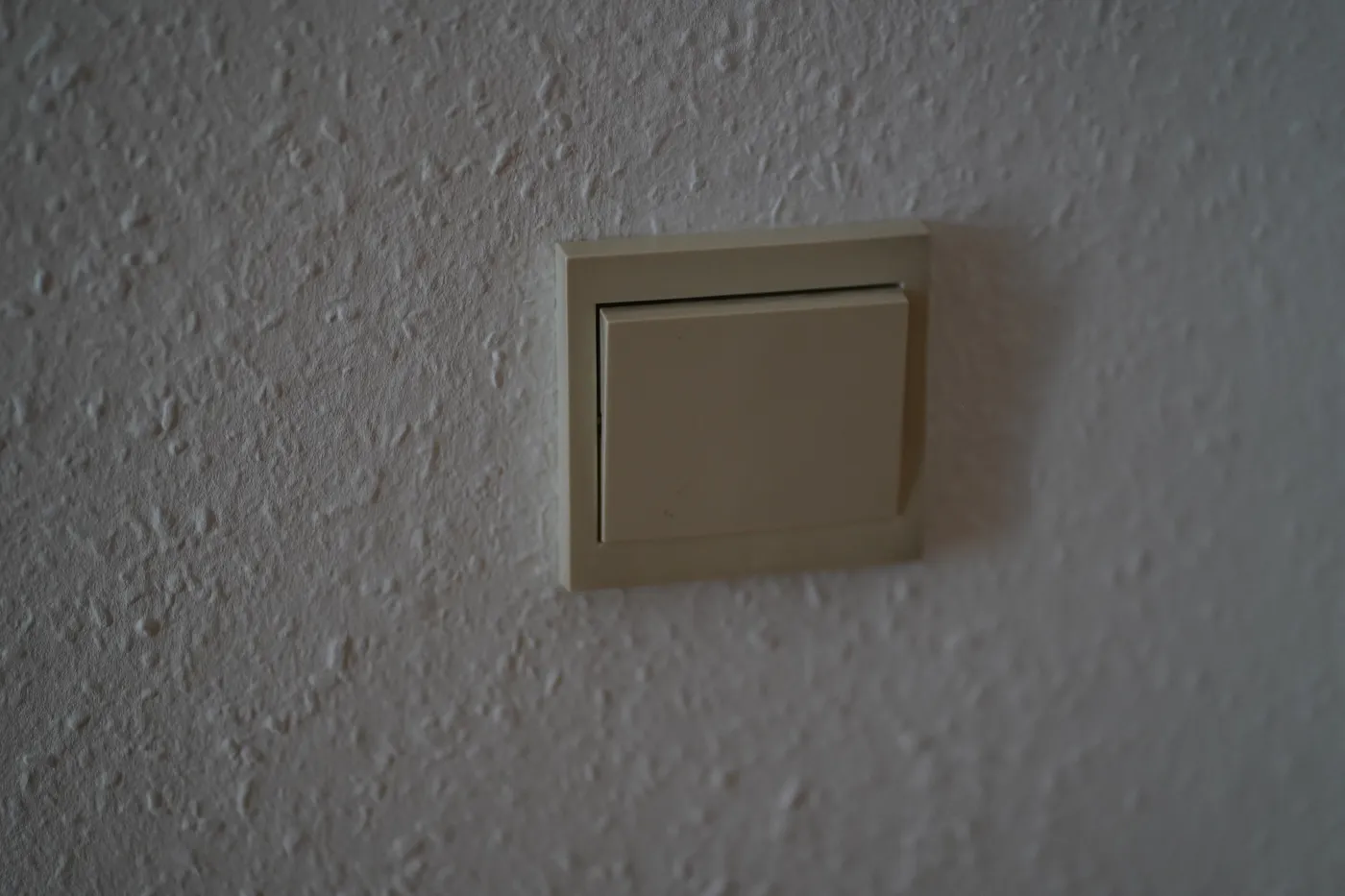 A single light switch on a textured white wall