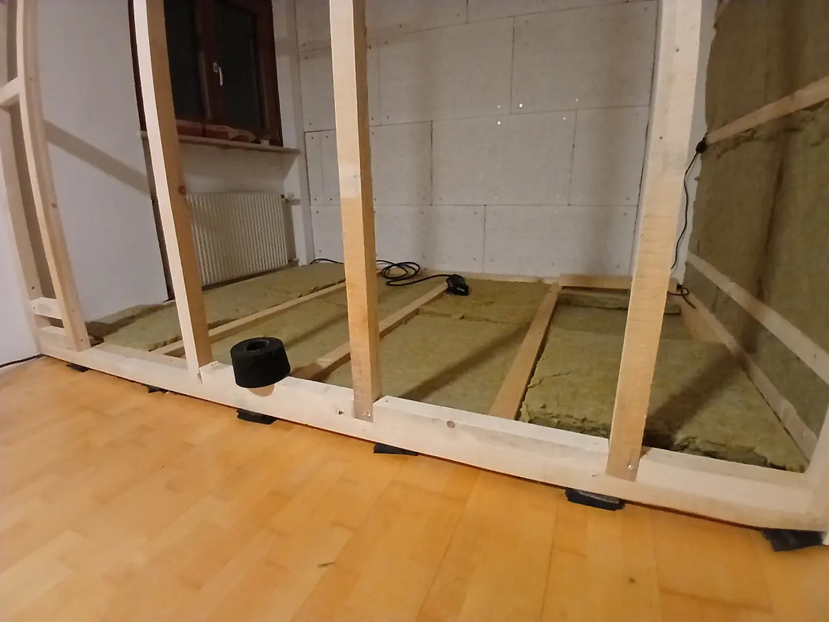 A timber stud frame standing in an empty room, insulation laid into the floor bays