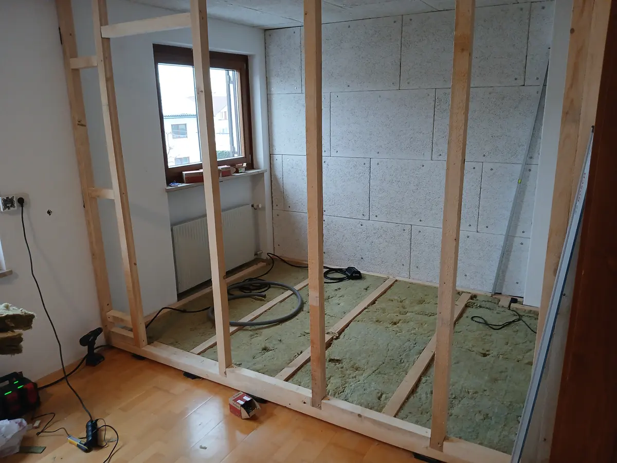 The timber frame with its first wall boarded out, mineral wool laid between the floor joists