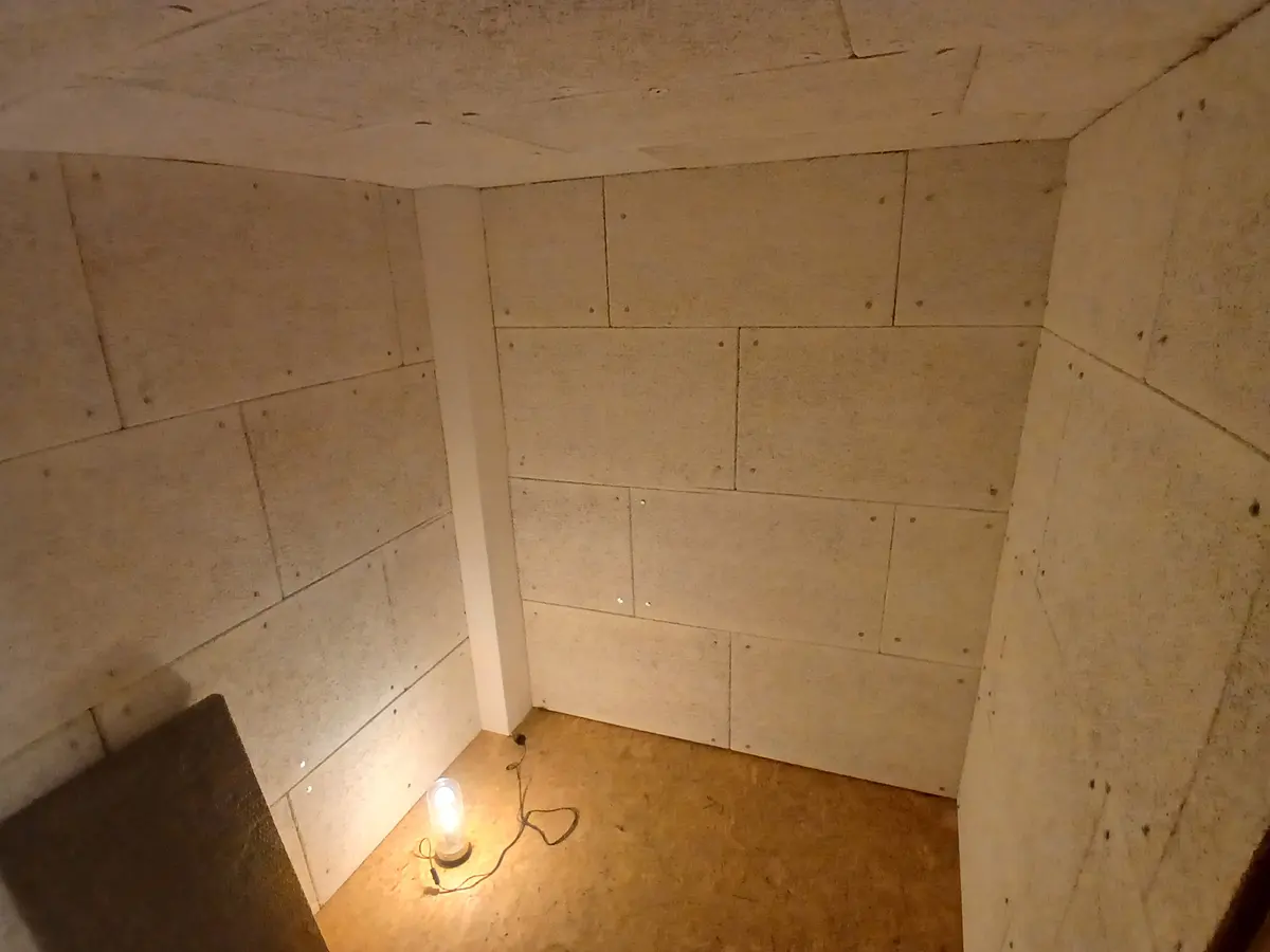 The finished inner shell, OSB on every wall, lit by a single work lamp on the floor
