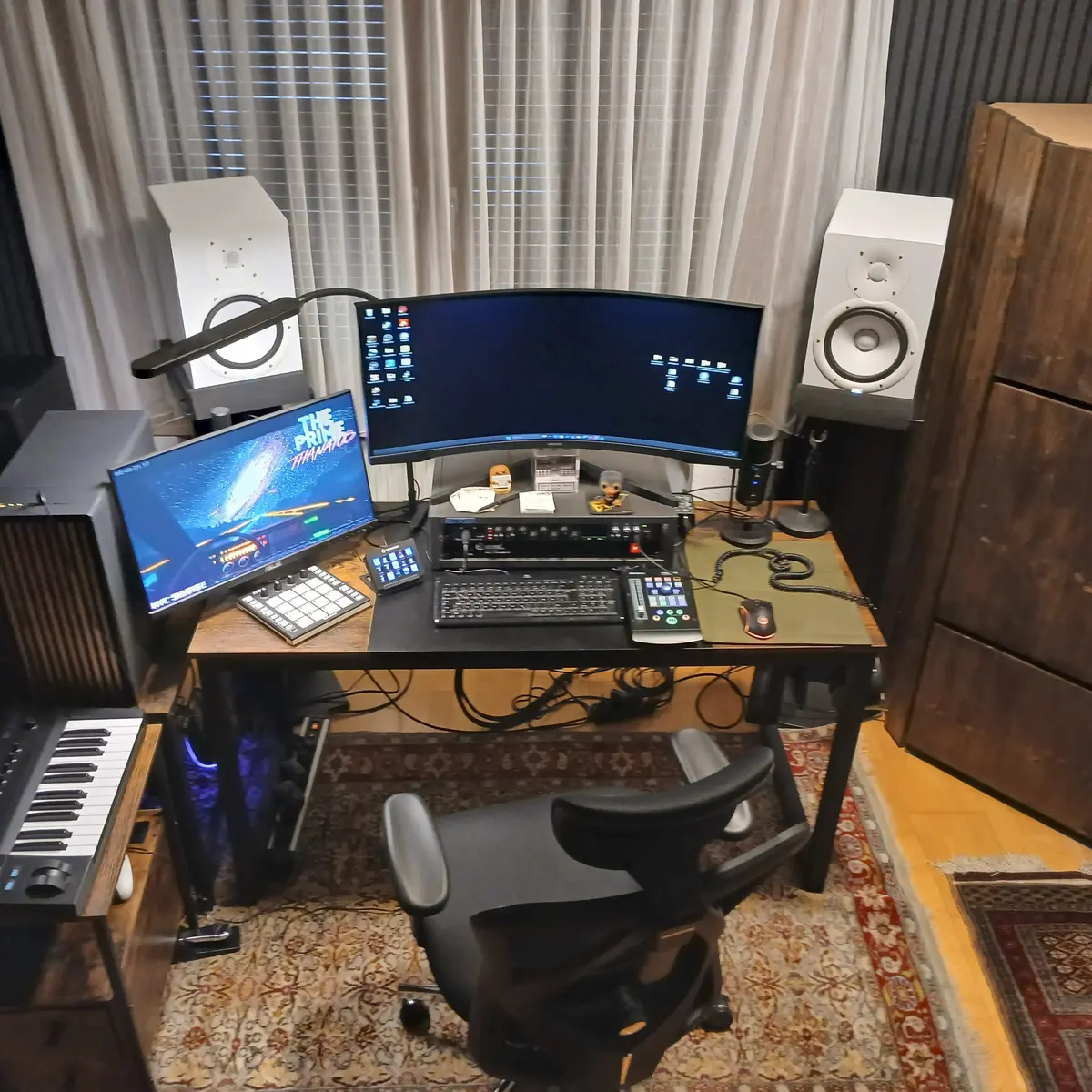 The studio today: a curved monitor between two nearfield speakers, a keyboard and a control surface on the desk, wood panelling behind